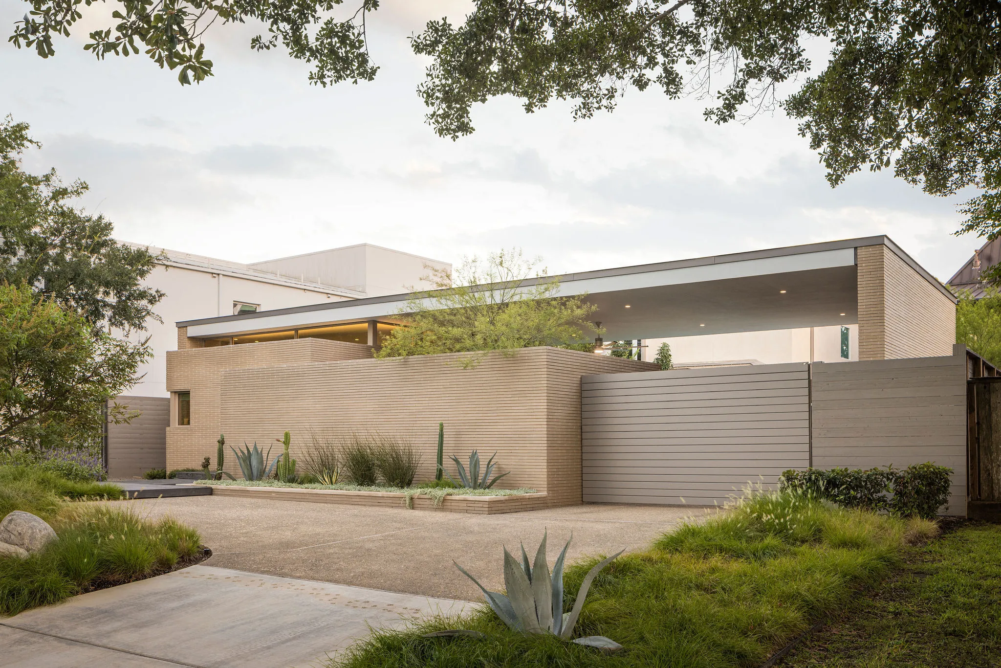 Low-slung pool house of textured tan brick with a deep flat-roof overhang, set behind a cactus and agave garden