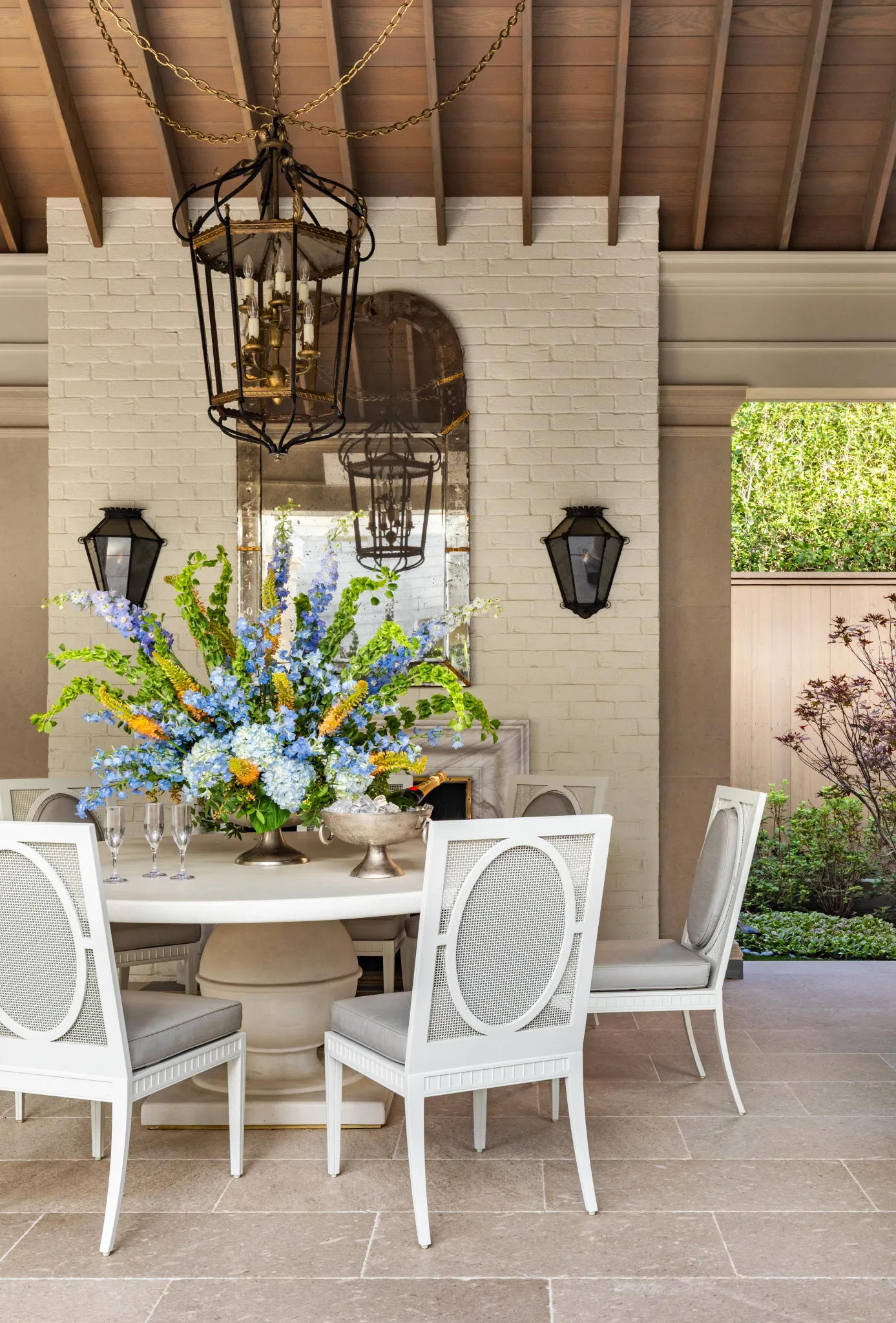 Round dining table beneath an iron lantern, with an antique mirror and sconces on white brick