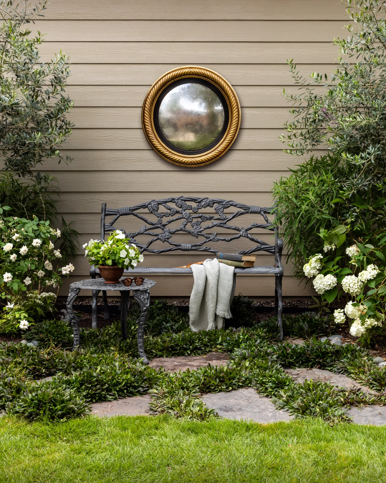 Iron garden bench beneath a gilt convex mirror, framed by white hydrangeas