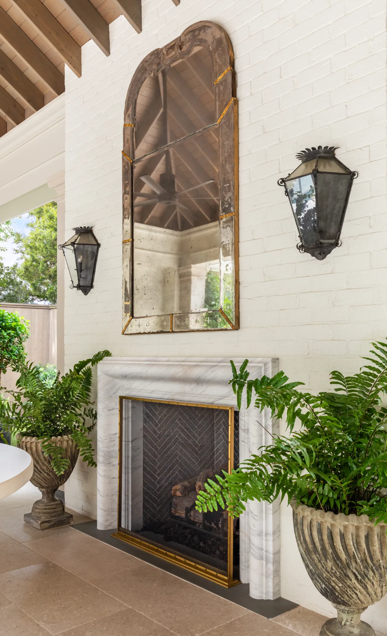 Marble fireplace beneath an arched antique mirror flanked by iron lanterns