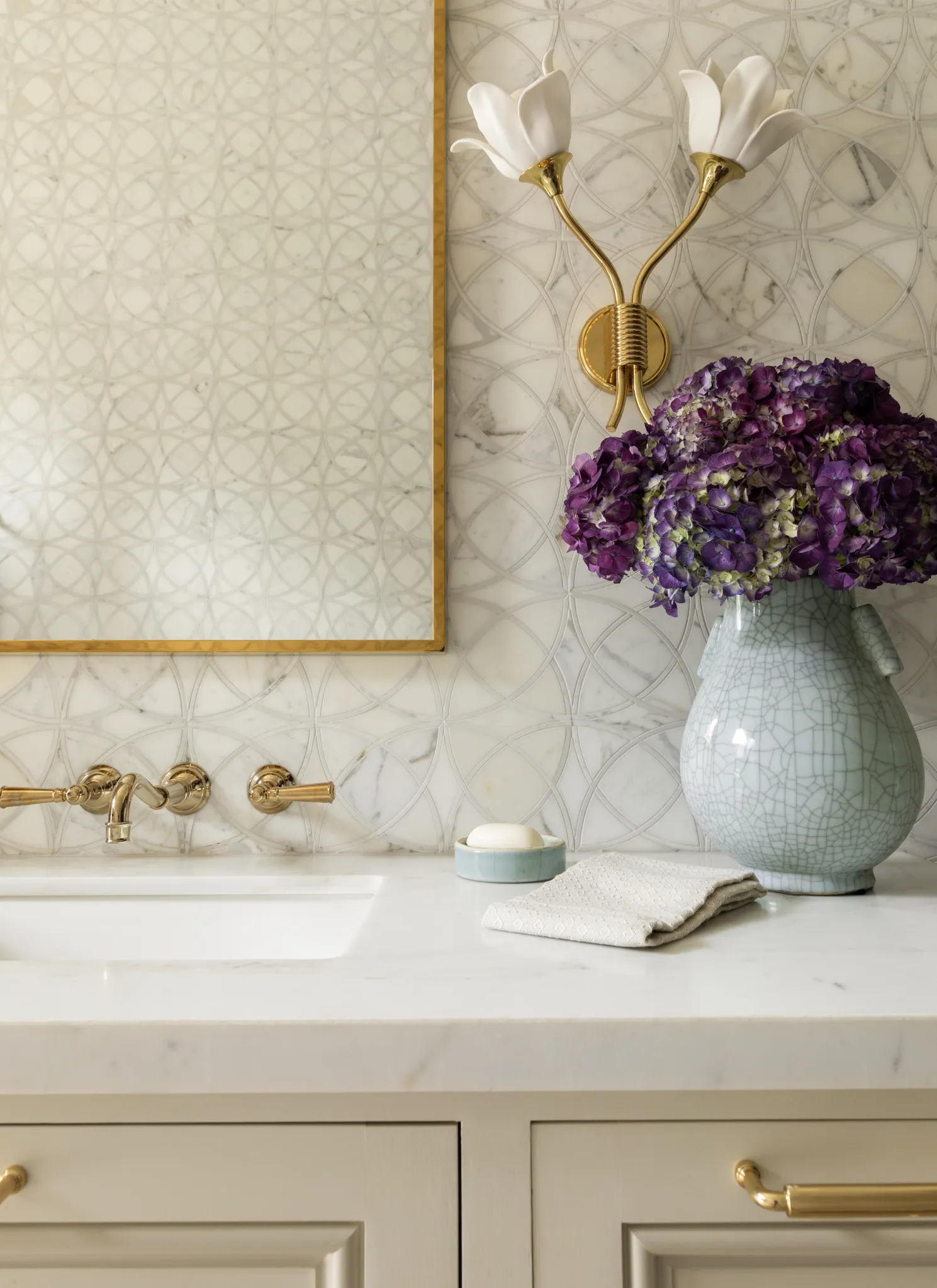 Vanity detail with brass fixtures, magnolia sconce, and hydrangeas in a crackle-glaze vase